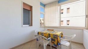 Un comedor con una mesa y sillas, una ventana con persianas y vistas a edificios.