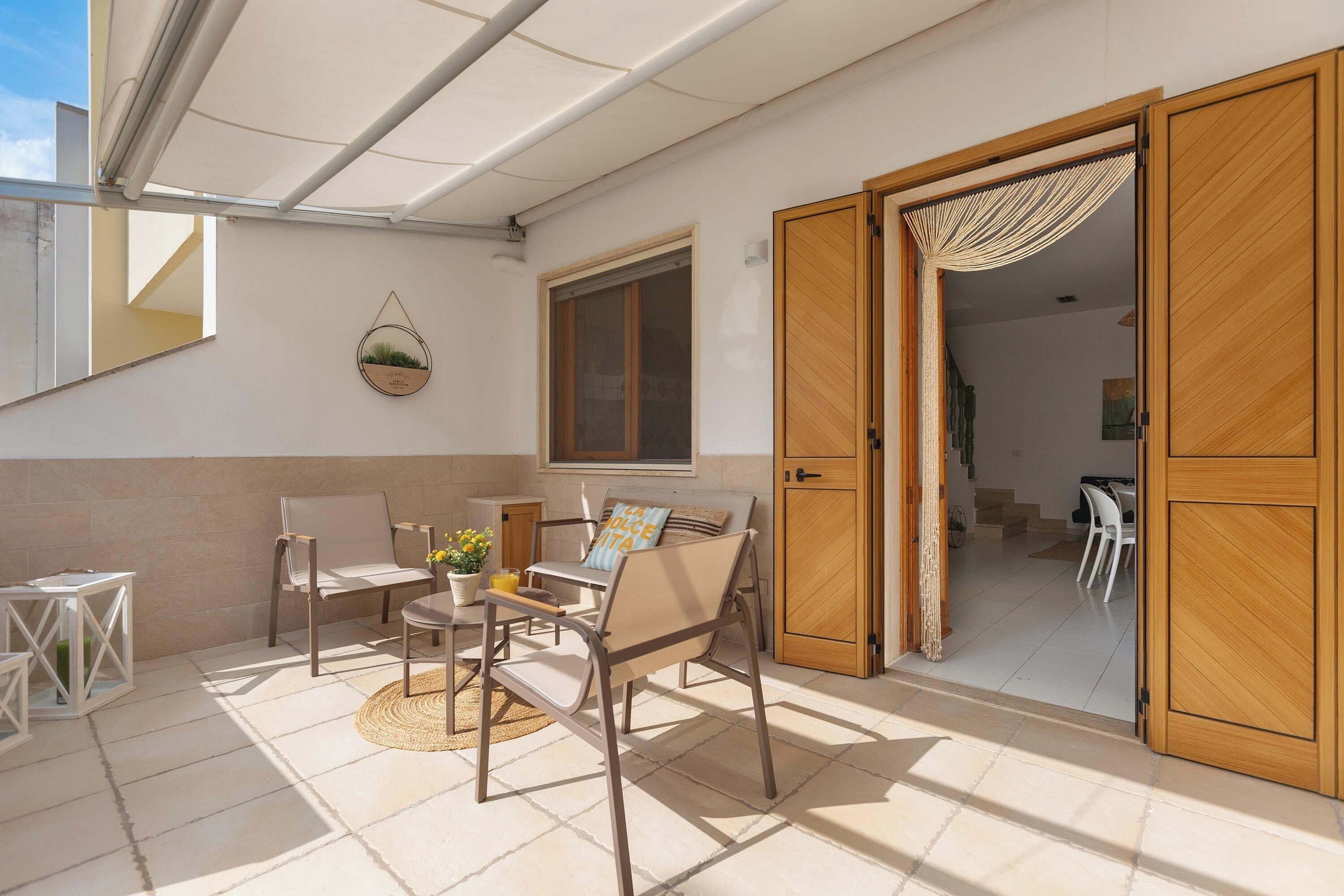 Une terrasse ensoleillée avec une table, des chaises et une porte en bois donnant sur un espace intérieur.