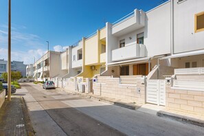 Uma fileira de edifícios residenciais modernos, com duas andares, varandas, portão e céu limpo.