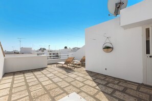 Terraço no telhado com parede branca, antena parabólica, planta pendente e duas cadeiras de lounge.