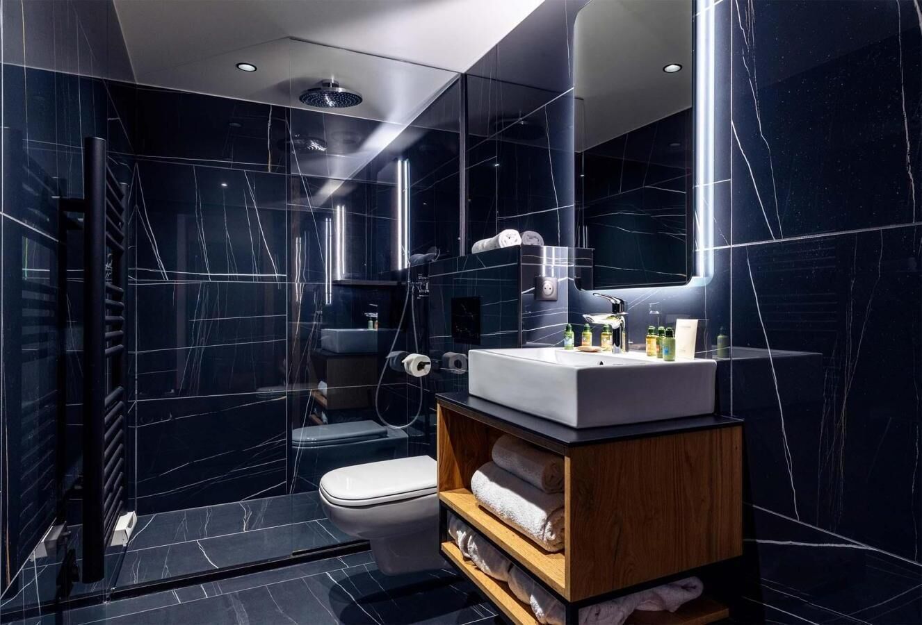 Une salle de bain moderne avec des carreaux de marbre foncé, un lavabo blanc et un meuble-lavabo en bois.