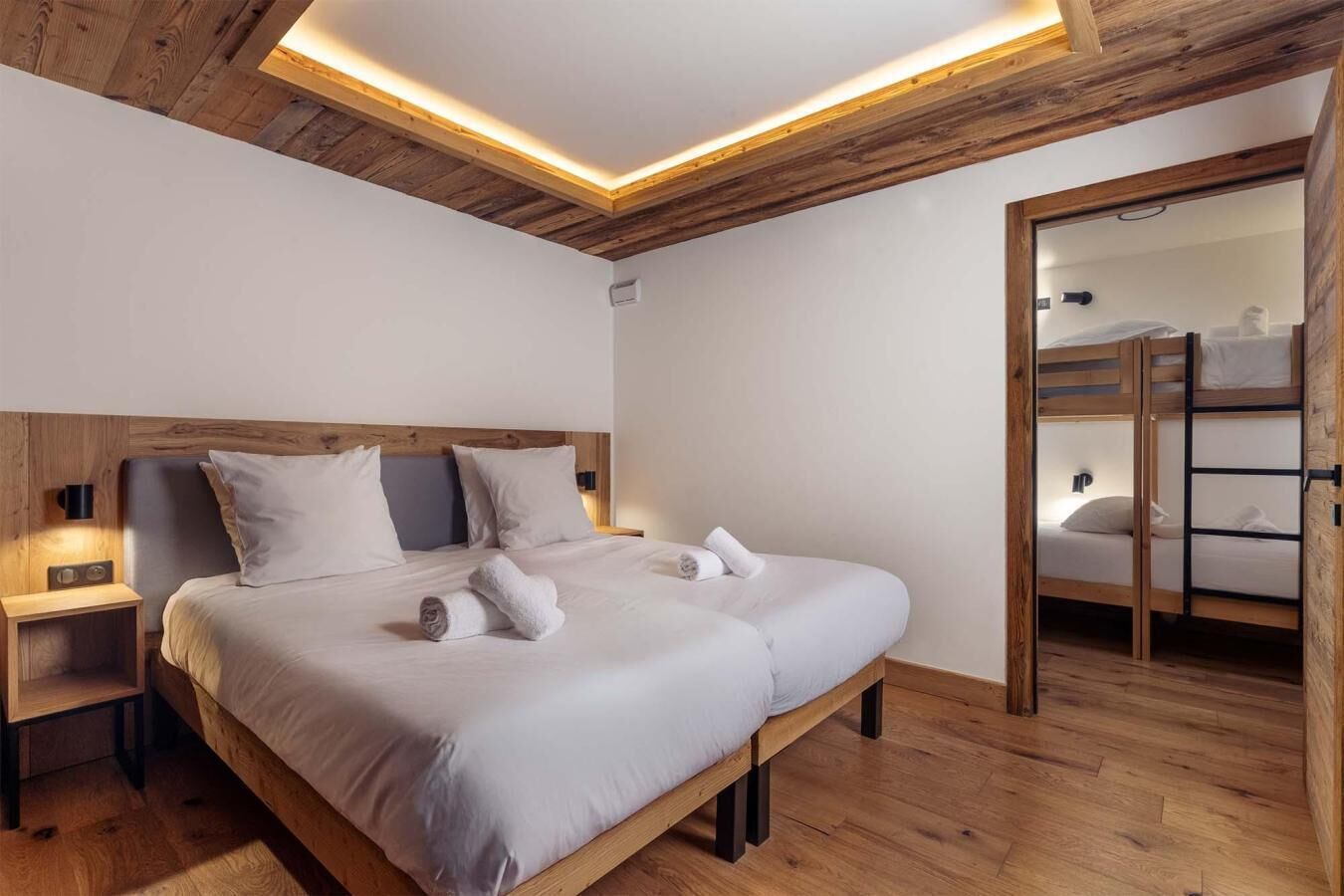 Una camera da letto moderna con soffitto in legno, un letto grande con lenzuola bianche, un comodino e una panca integrata con uno specchio.