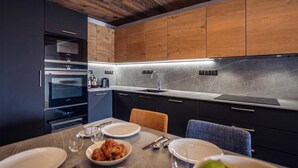 A modern kitchen with dark cabinetry, a wooden ceiling, and a marble backsplash.