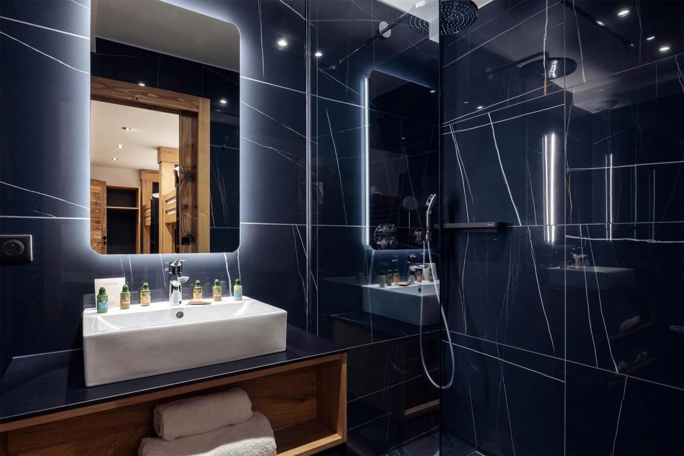 Ein modernes Badezimmer mit Waschbecken, Spiegel und dunkel gefliesten Wänden.