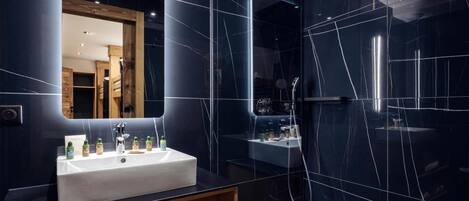 Ein modernes Badezimmer mit Waschbecken, Spiegel und dunkel gefliesten Wänden.