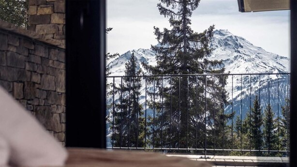 A room with a stone wall and a view of a snow-covered mountain through a balcony railing.