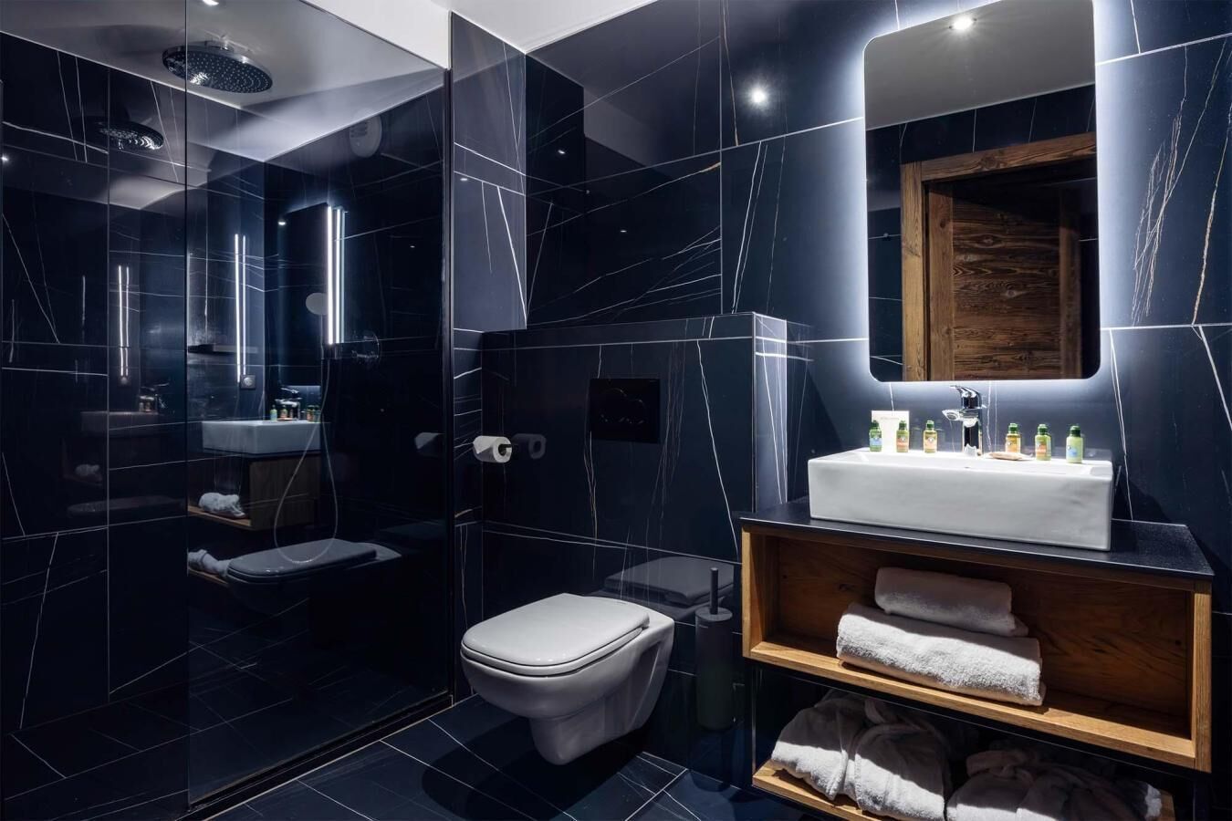 Une salle de bain moderne avec une douche à parois de verre, des toilettes blanches, un meuble-lavabo avec un miroir et une étagère avec des serviettes.