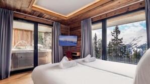 Una habitación de hotel moderna con una cama grande, techo de madera, televisor y un balcón con vistas a la montaña.