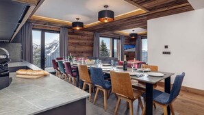 Una cocina moderna con una isla grande, comedor con sillas de madera y amplias ventanas con vistas a la montaña.