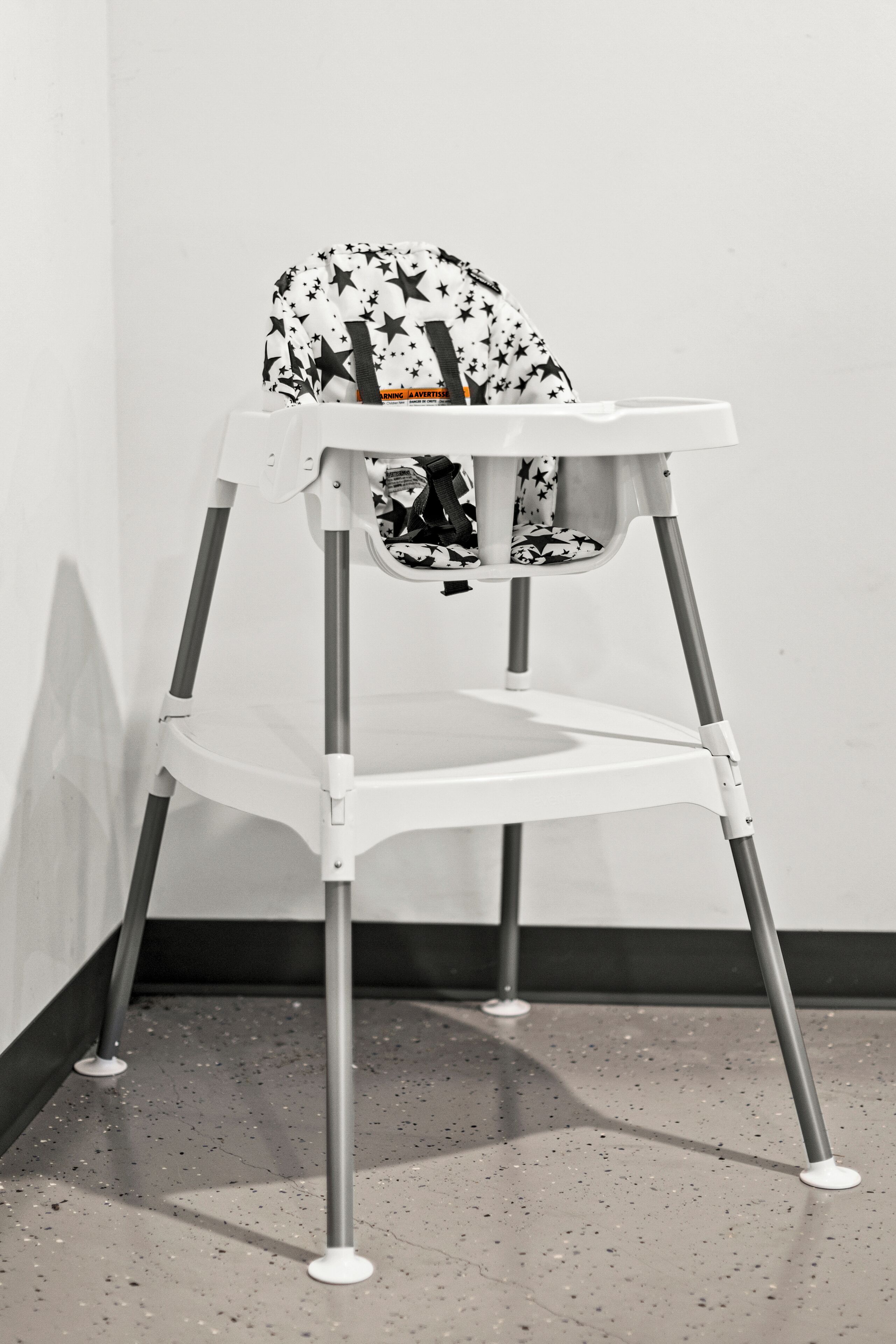A white high chair with a star pattern, positioned against a plain wall.