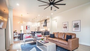 A modern living room with a leather sofa, a coffee table, and a TV. There is a kitchen in the background with a ceiling fan. - Spacious 3-bedroom house in Central Lubbock (Lubbock)