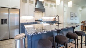A modern kitchen with white cabinets, a stainless steel refrigerator, a large island with bar stools, and pendant lighting. - Spacious 3-bedroom house in Central Lubbock (Lubbock)