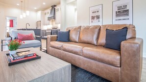 A modern living room with a leather sofa, a coffee table with books, and a kitchen in the background. - Spacious 3-bedroom house in Central Lubbock (Lubbock)