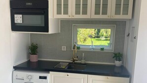 A compact kitchen with a built-in washing machine, a microwave, and a window with a view of greenery.