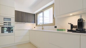 A modern kitchen with white cabinetry, a built-in oven, a coffee machine, and a window above the sink. - 217 Le Jungle in Cannes (Cannes)