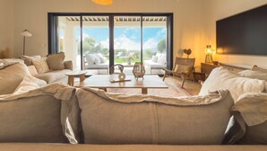 A spacious living room with a large sofa, a coffee table, and a view through large sliding doors to an outdoor area. - Villa Maeva in Cavalaire-sur-mer (Cavalaire-sur-Mer)
