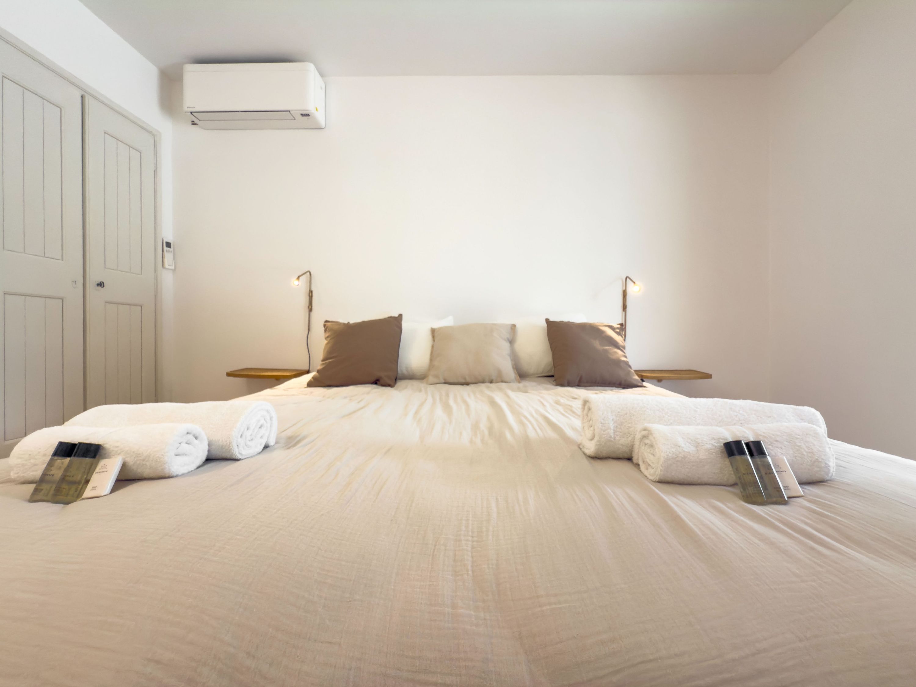 Una cama bien hecha con almohadas y toallas, una mesita de noche con lámpara y un equipo de aire acondicionado en la pared.