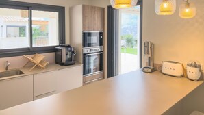 A modern kitchen with a large window, stainless steel appliances, and hanging pendant lights. - Villa Maeva in Cavalaire-sur-mer (Cavalaire-sur-Mer)