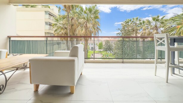 A balcony with a white sofa, a dining table, and a chair. There is a view of palm trees and a building in the background. - 213 Le Montfleury in Cannes (Cannes)