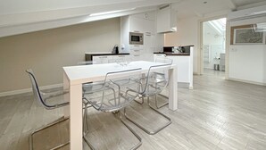 A modern kitchen with white cabinets, a central island, and a dining area with a white table and clear chairs. - 210 - Tony Allard 4A (Cannes)