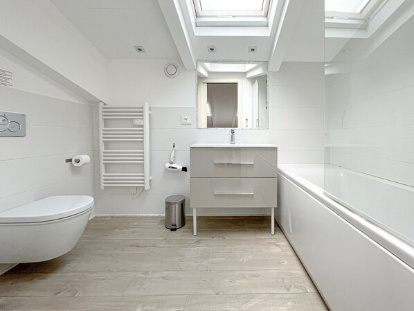Ein modernes Badezimmer mit Oberlicht, weißen Armaturen und Holzboden.