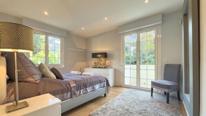 Ein modernes Schlafzimmer mit einem großen Bett, Nachttischen, einem Schreibtisch und einem Stuhl. Eine Glastür führt auf einen Balkon.