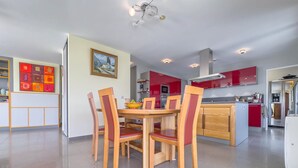 A modern kitchen with red cabinets, a dining area with wooden chairs, and a tiled floor. - Le Rooftop in Cannes (Cannes)