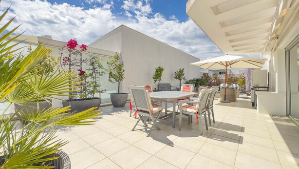 An outdoor patio area with a dining table and chairs, surrounded by potted plants and a large umbrella. - Le Rooftop in Cannes (Cannes)
