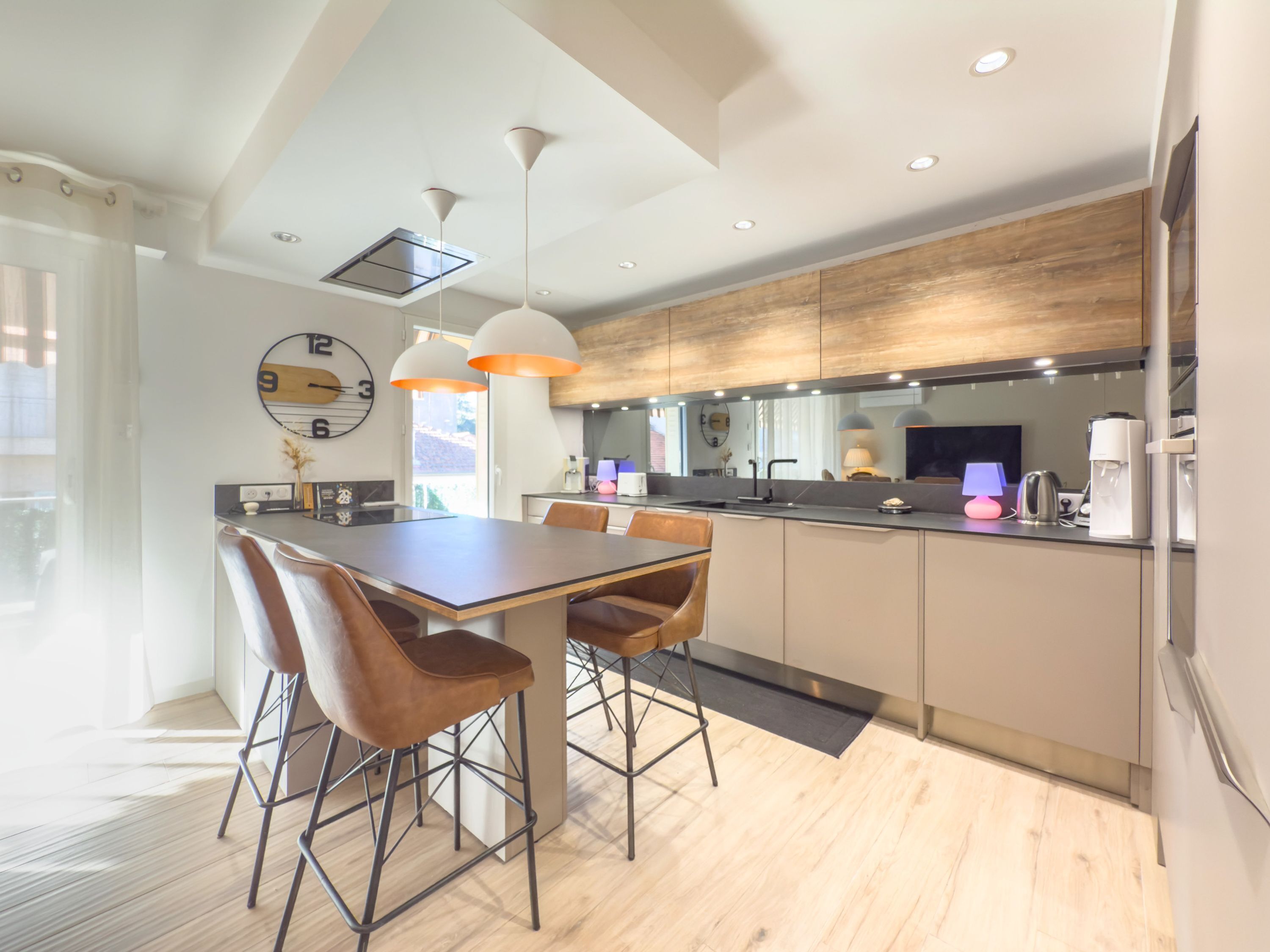 Een moderne keuken met een centraal eiland, hanglampen en een groot raam.