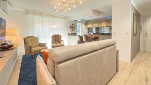 A modern living room with a sofa, chairs, a dining table, and a kitchen in the background.