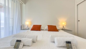 A hotel room with a large bed, two nightstands with lamps, and a window with sheer curtains.