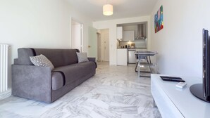 A modern living room with a grey sofa, a dining table, and a kitchen area in the background.