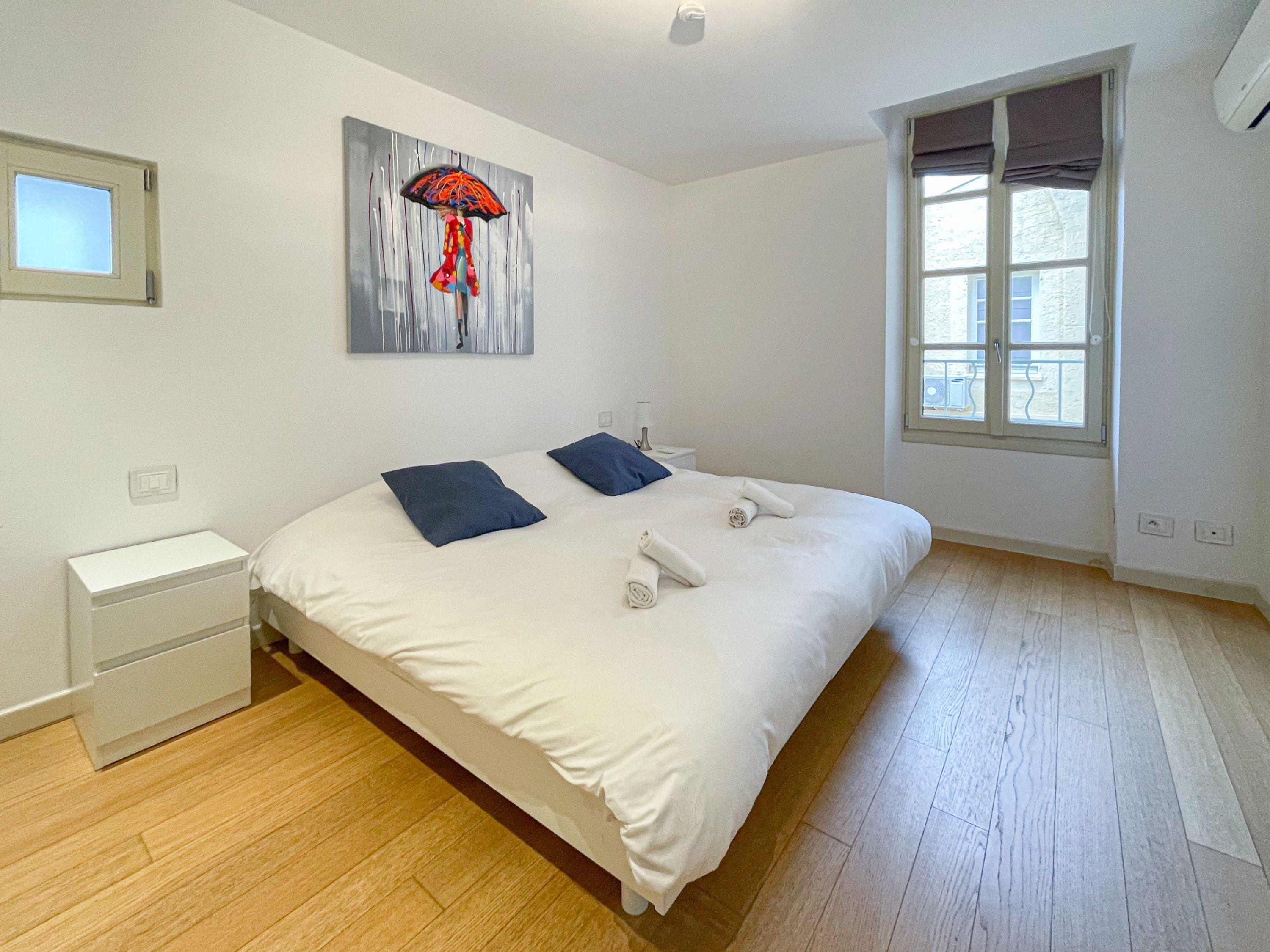 A bedroom with a large bed, two pillows, a nightstand, a wall art piece, and a window.