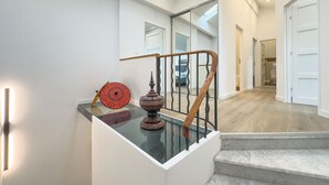 A modern interior with a glass railing, a decorative item, and a view into a room with a bed and a door.
