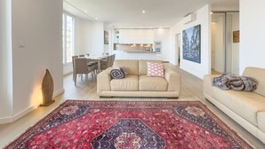 Ett modernt vardagsrum med en beige soffa, en mönstrad matta och en matplats med ett bord och stolar.