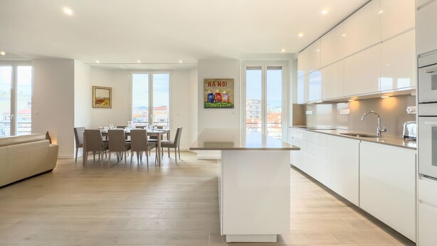 A modern kitchen with white cabinets, a central island, and a dining area with chairs and a table.