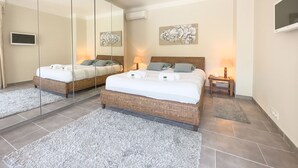 Ett modernt hotellrum med två sängar av rotting, grå mattor och konstverk på väggarna.