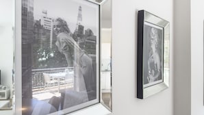 Ett inramat fotografi av en kvinna mot en stadsbild, upphängt på en vit vägg.