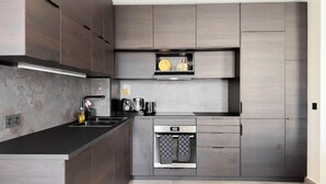 A modern kitchen with dark wood cabinetry, a black countertop, a built-in oven, and a coffee machine. - 100 Le Riviera in Cannes (Cannes)
