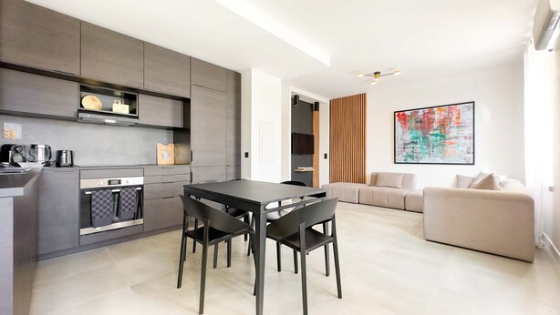 A modern kitchen with dark cabinetry, a dining table with chairs, a sofa, and a large abstract painting on the wall. - 100 Le Riviera in Cannes (Cannes)