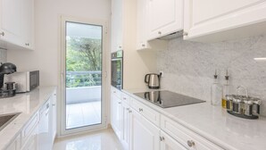 Una cocina moderna con armarios blancos, horno de acero inoxidable, placa de inducción negra y puerta de vidrio que da a un balcón.
