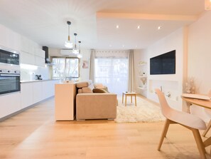 A modern kitchen with white cabinets, a built-in oven, and a dining area with a white sofa and a small table.
