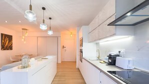 Una cocina moderna con armarios blancos, una isla central, iluminación colgante y un horno empotrado.