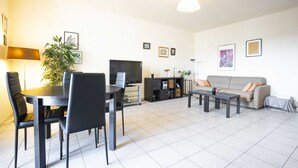 Ein Wohnzimmer mit Esstisch, Stühlen, einer Couch, einem Fernseher und einer Pflanze.