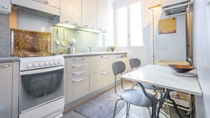 Eine moderne Küche mit Einbauofen, Herd und Mikrowelle. Ein Esstisch mit Stühlen und eine kleine Kücheninsel mit einer Schüssel sind ebenfalls vorhanden.