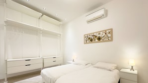 A bedroom with a large bed, two bedside tables with lamps, a wardrobe with multiple drawers, an air conditioning unit, and a decorative wall piece. - 2A Tony Allard in Cannes (Cannes)