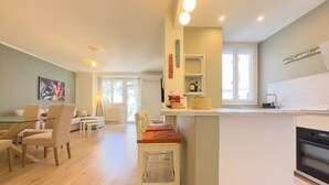 Eine moderne Küche mit Kochinsel, ein Essbereich mit Glastisch und ein Wohnzimmer mit Sofa und Sesseln.