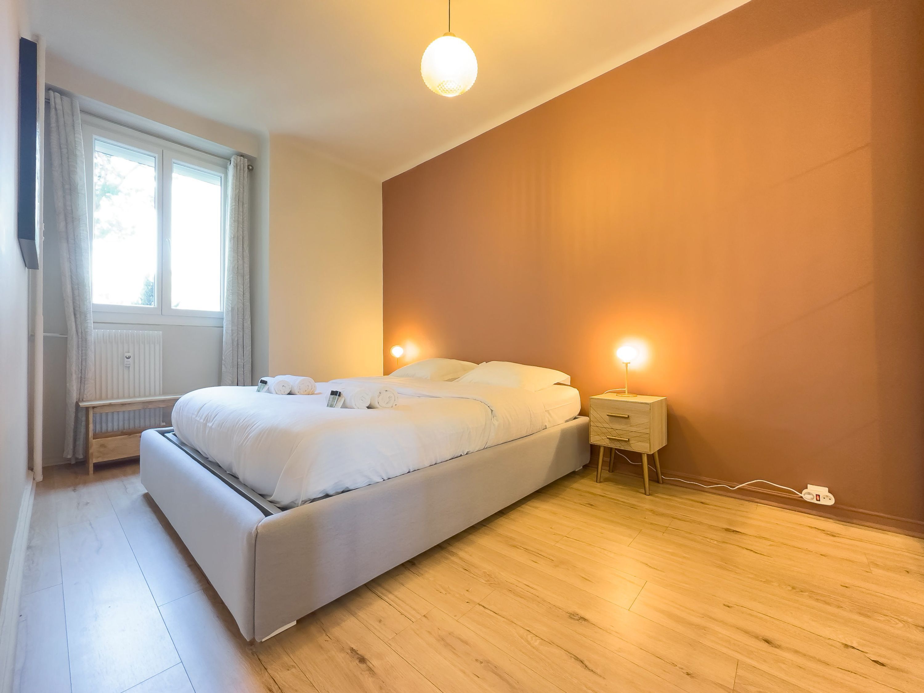 Ein modernes Schlafzimmer mit einem großen Bett, Nachttischen und einem Fenster mit Vorhängen.