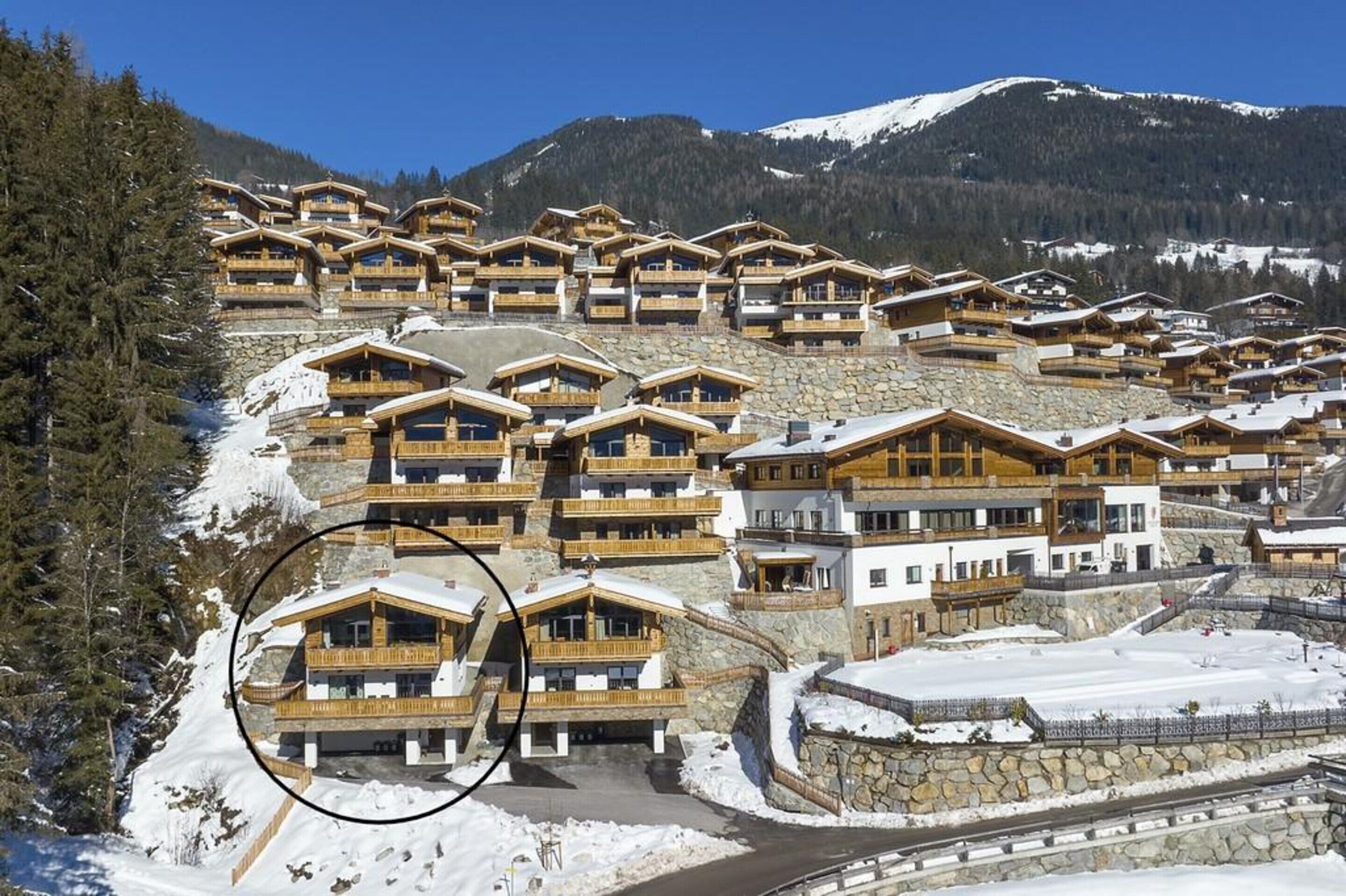 A cluster of wooden chalets with balconies, set against a snowy mountain backdrop.