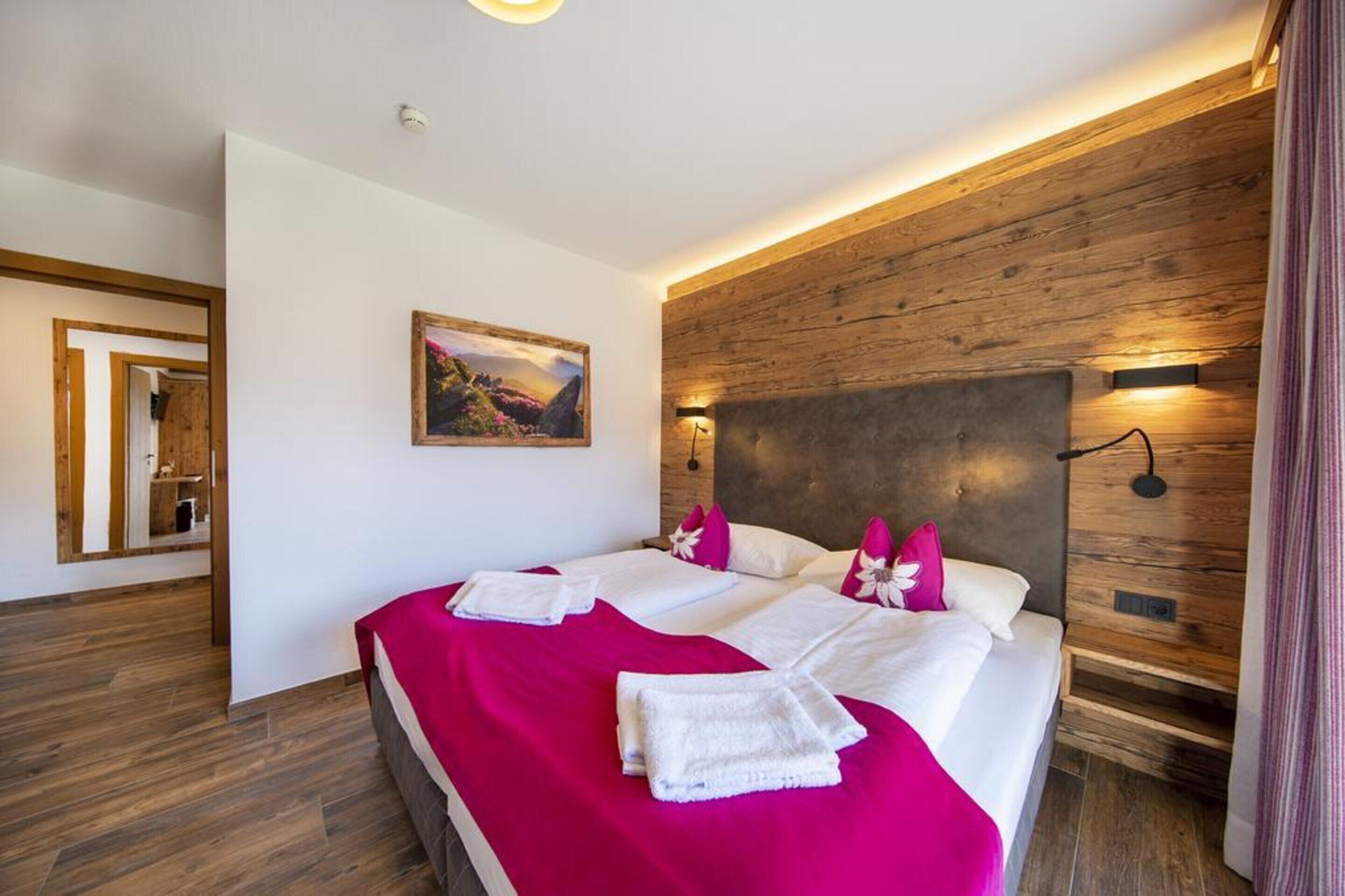 A modern hotel room with a large bed, wooden headboard, and a painting on the wall.